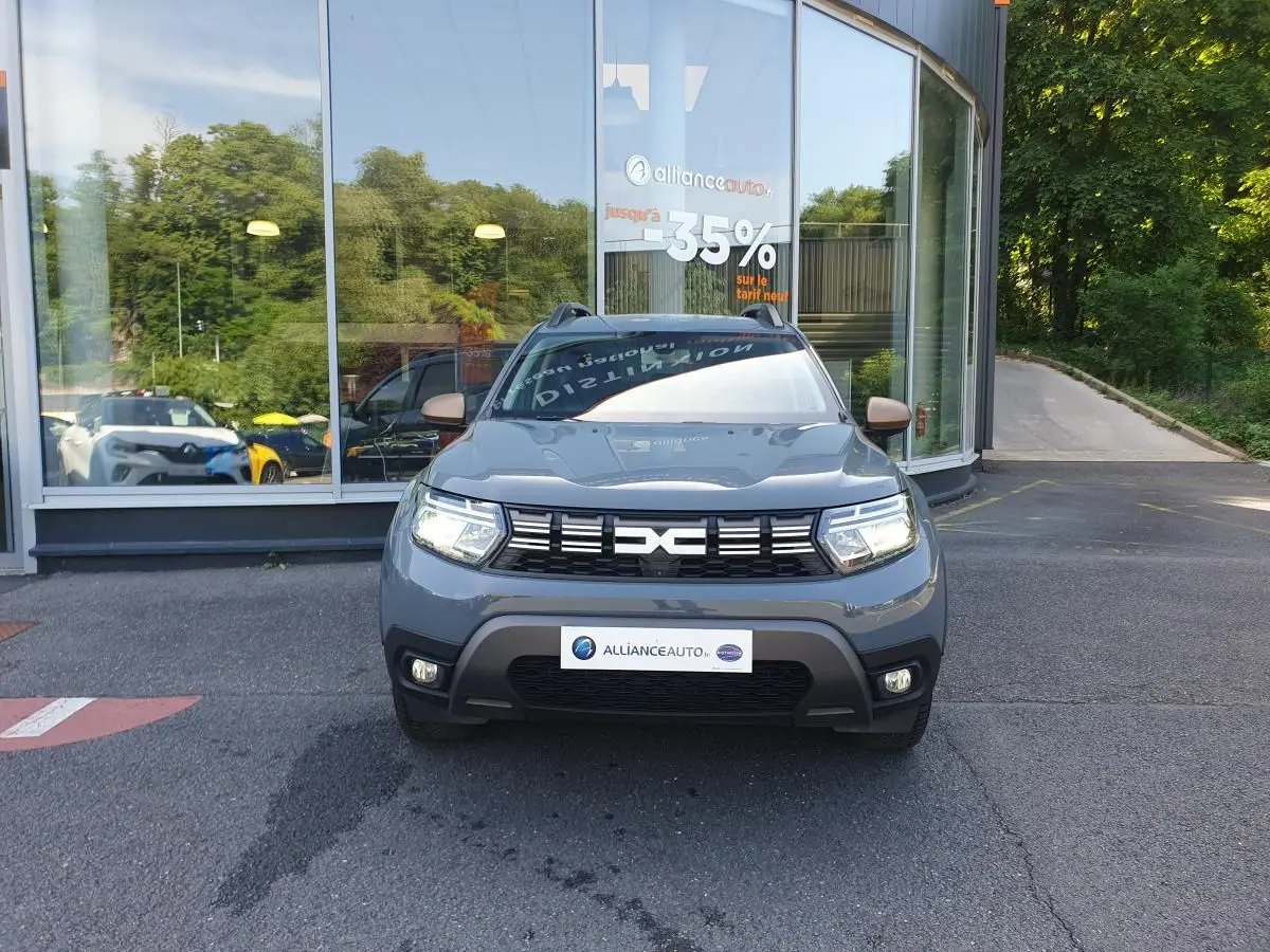 Dacia Duster gris urbain vue de face, avec calandre noire et signature lumineuse LED allumée.