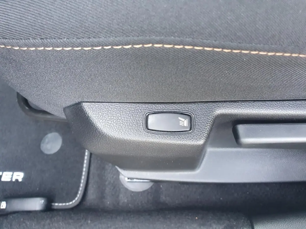 Détail du bouton de siège chauffant sur la partie inférieure d’un siège avant du Dacia Duster gris urbain 2023.