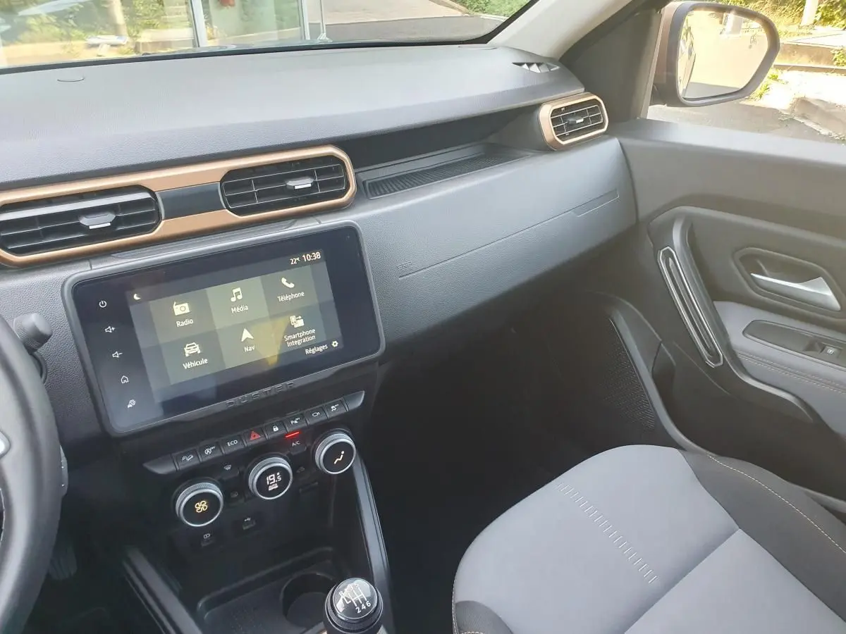 Vue intérieure côté passager du tableau de bord et console centrale du Dacia Duster gris urbain 2023 avec écran tactile et boîte manuelle.