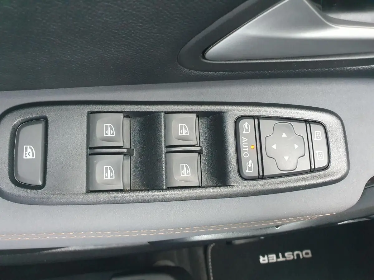 Gros plan sur les commandes des vitres électriques et rétroviseurs sur la porte côté conducteur du Dacia Duster gris urbain 2023.