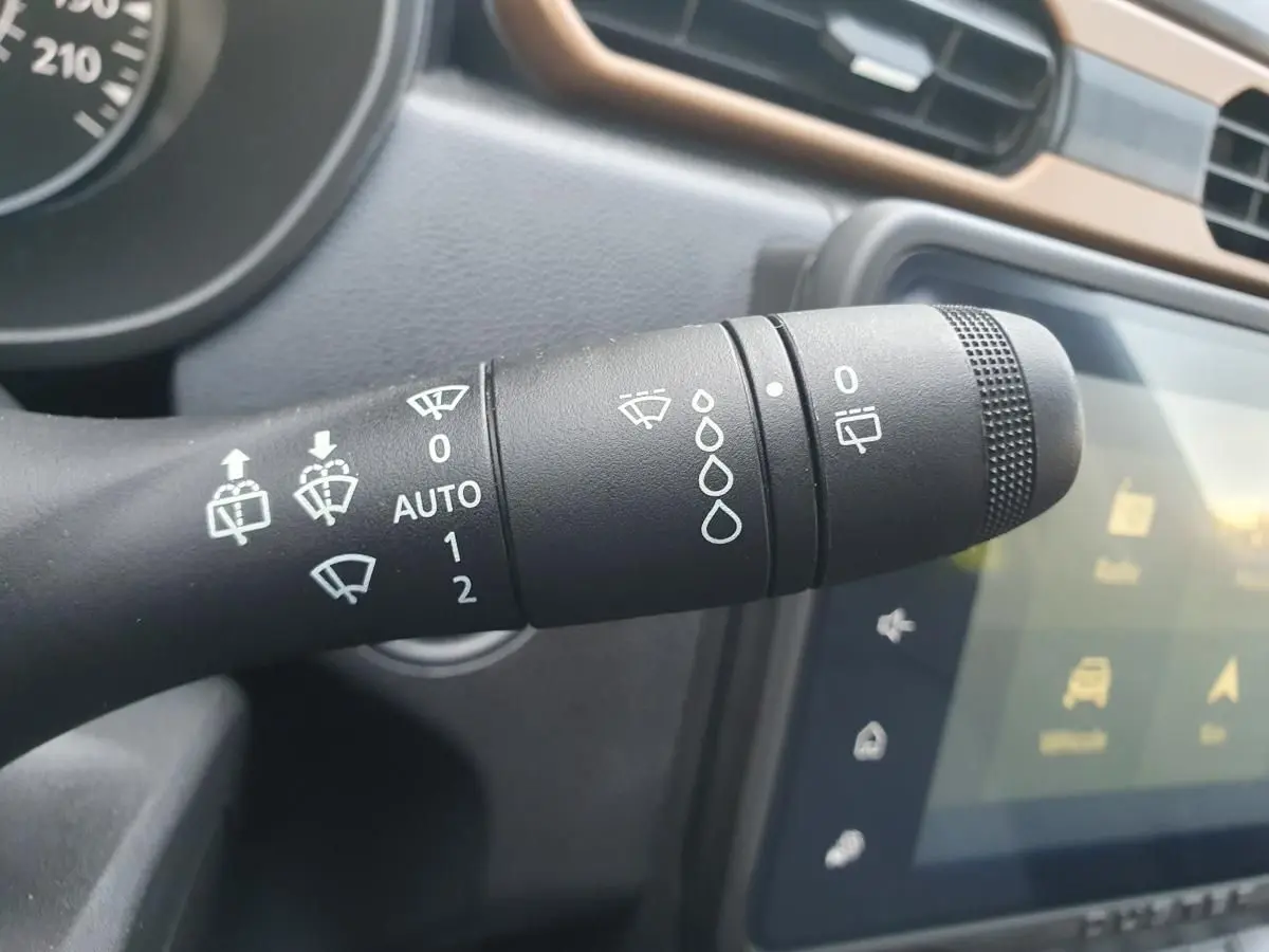 Gros plan sur la commande d’essuie-glace du Dacia Duster gris urbain, avec tableau de bord et écran tactile en arrière-plan.