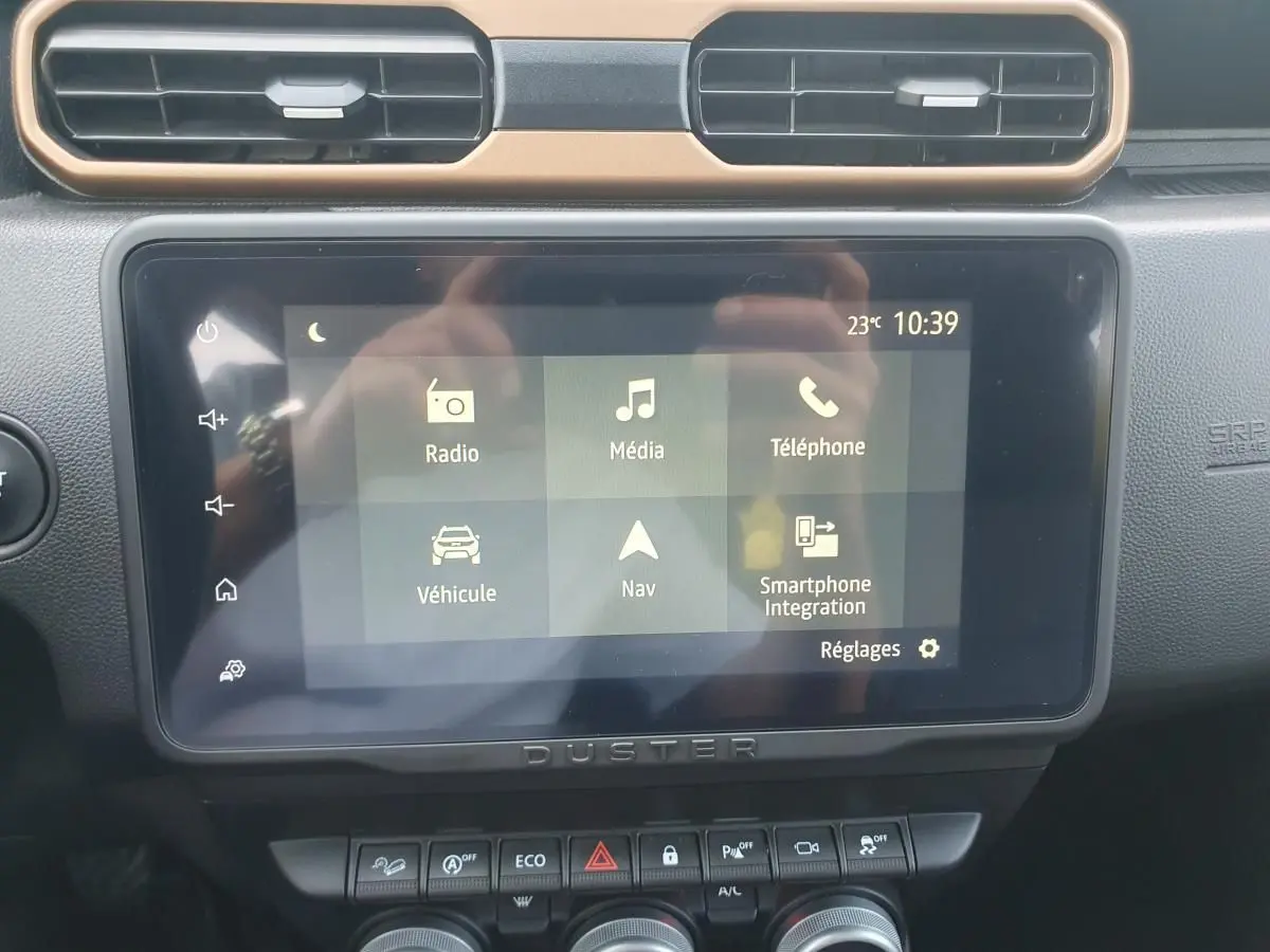 Écran tactile central du Dacia Duster 2023 avec interface multimédia et commandes sous l'écran, vue intérieure frontale.