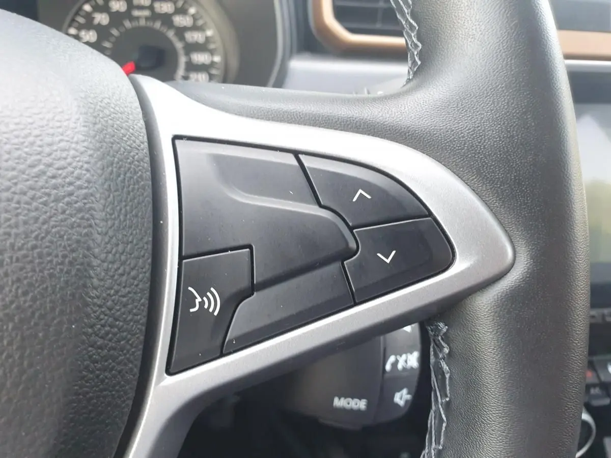 Gros plan sur les commandes du volant noir du Dacia Duster 2023, avec boutons de réglage et commande vocale.