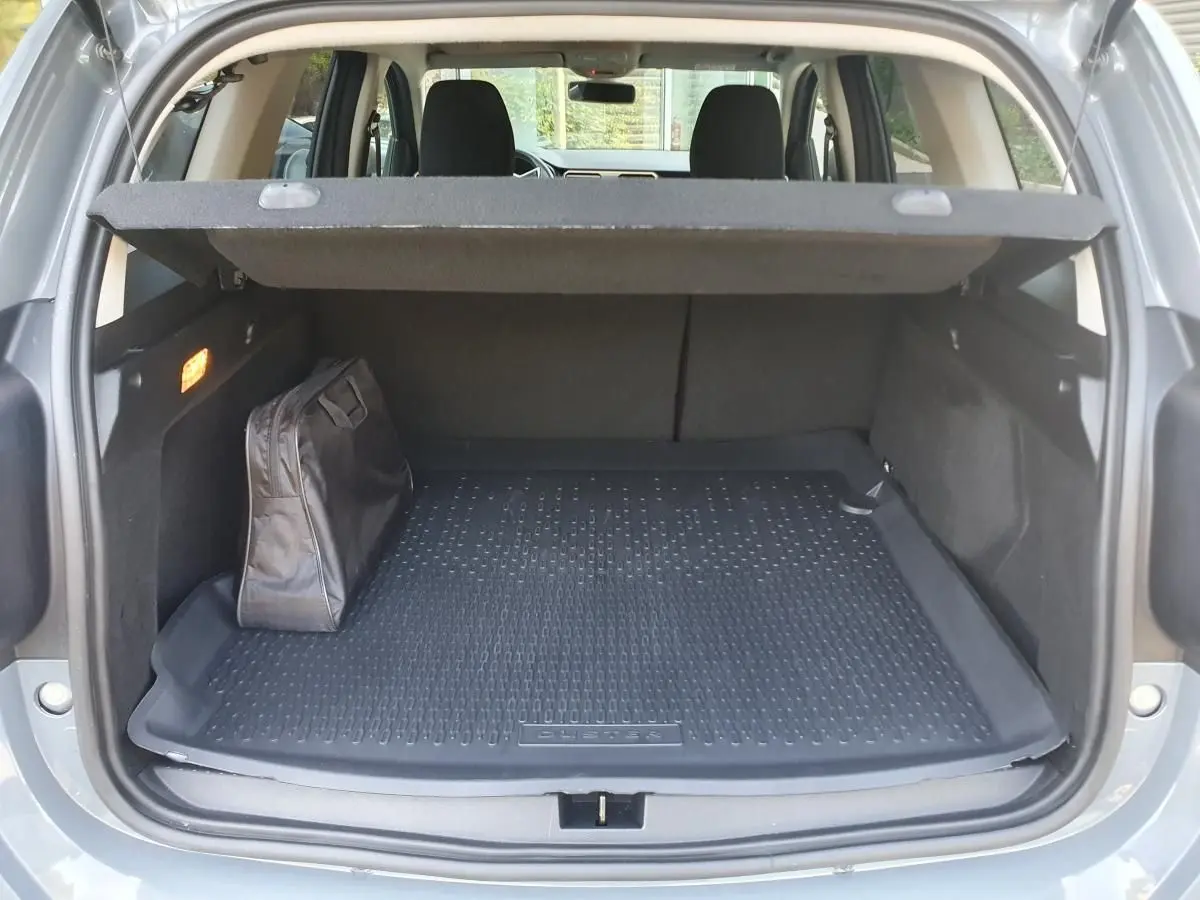 Coffre ouvert du Dacia Duster gris urbain 2023, avec tapis de protection et sac noir à gauche.