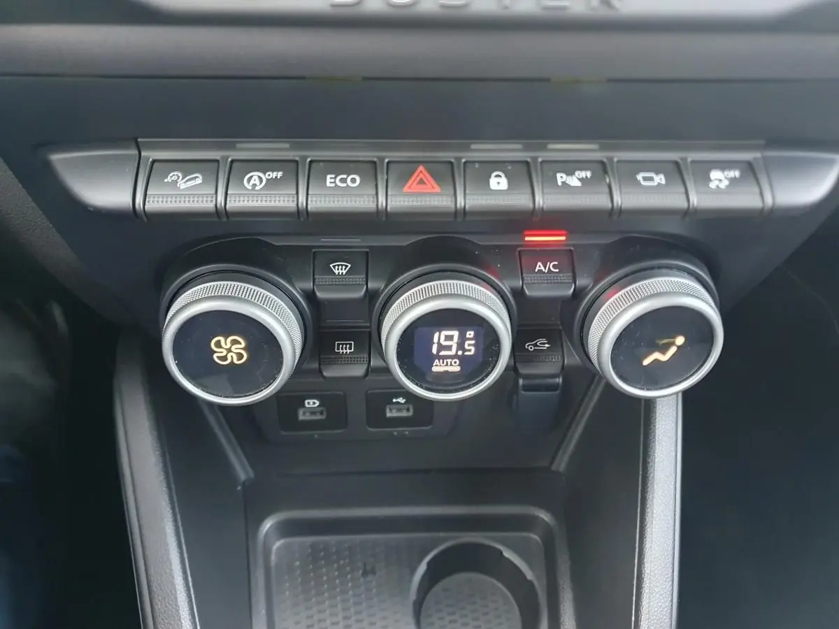 Vue rapprochée du tableau de bord du Dacia Duster 2023, montrant les commandes de climatisation automatique et les boutons de fonction.
