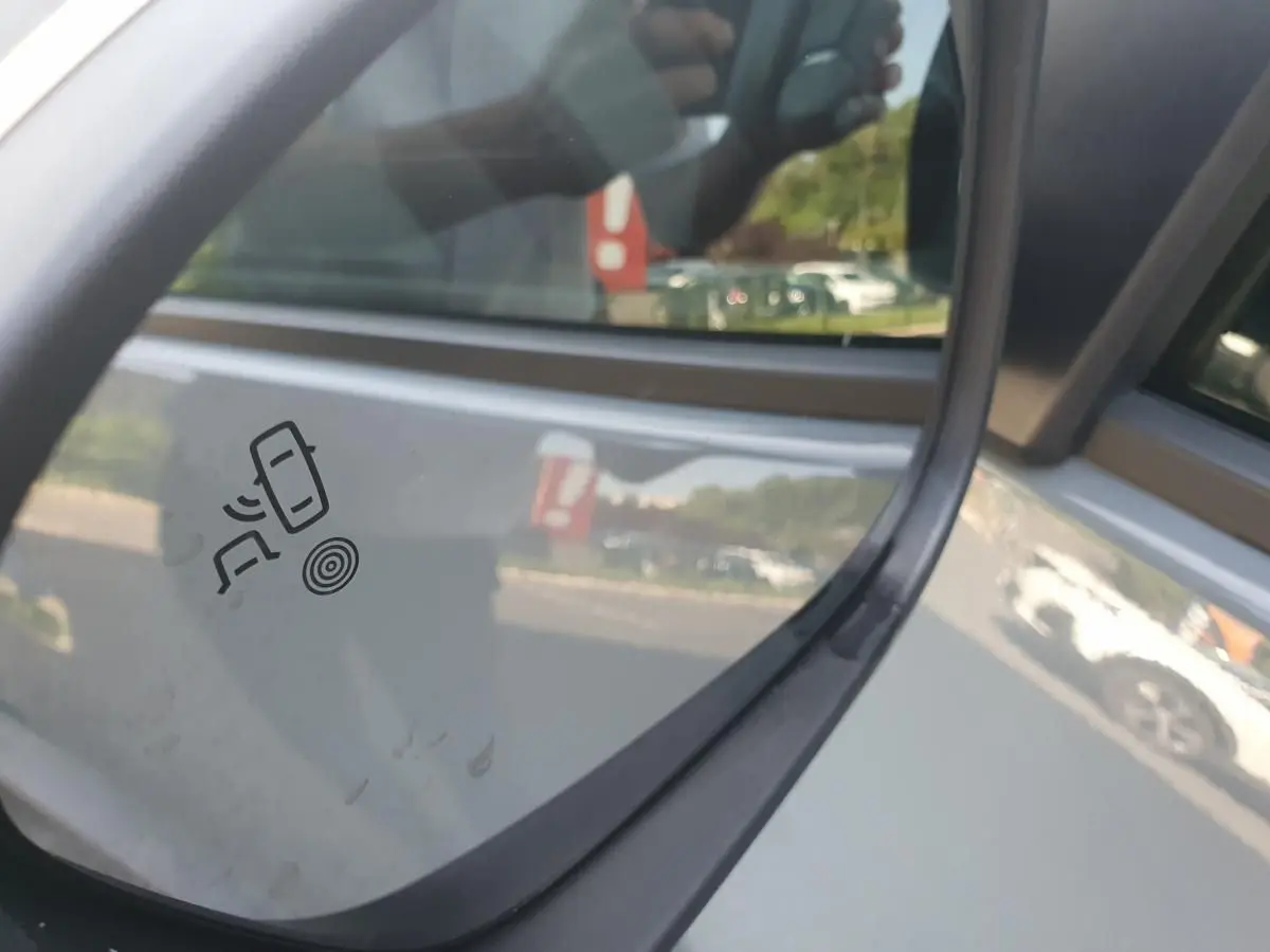 Gros plan sur le rétroviseur droit gris urbain du Dacia Duster 2023 avec pictogramme d’alerte d’angle mort visible.