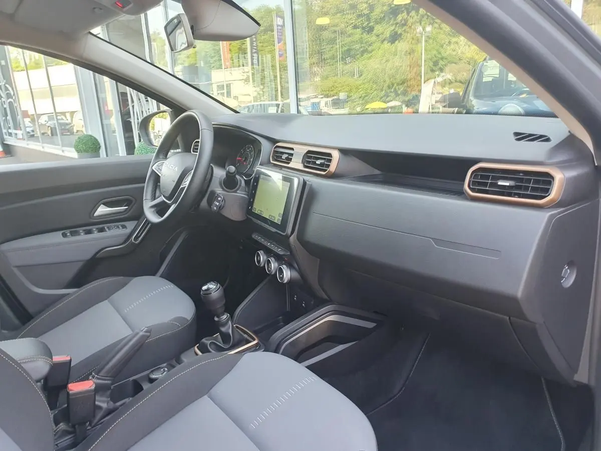 Intérieur du Dacia Duster 2023 gris urbain, vue côté conducteur avec tableau de bord et écran tactile central.