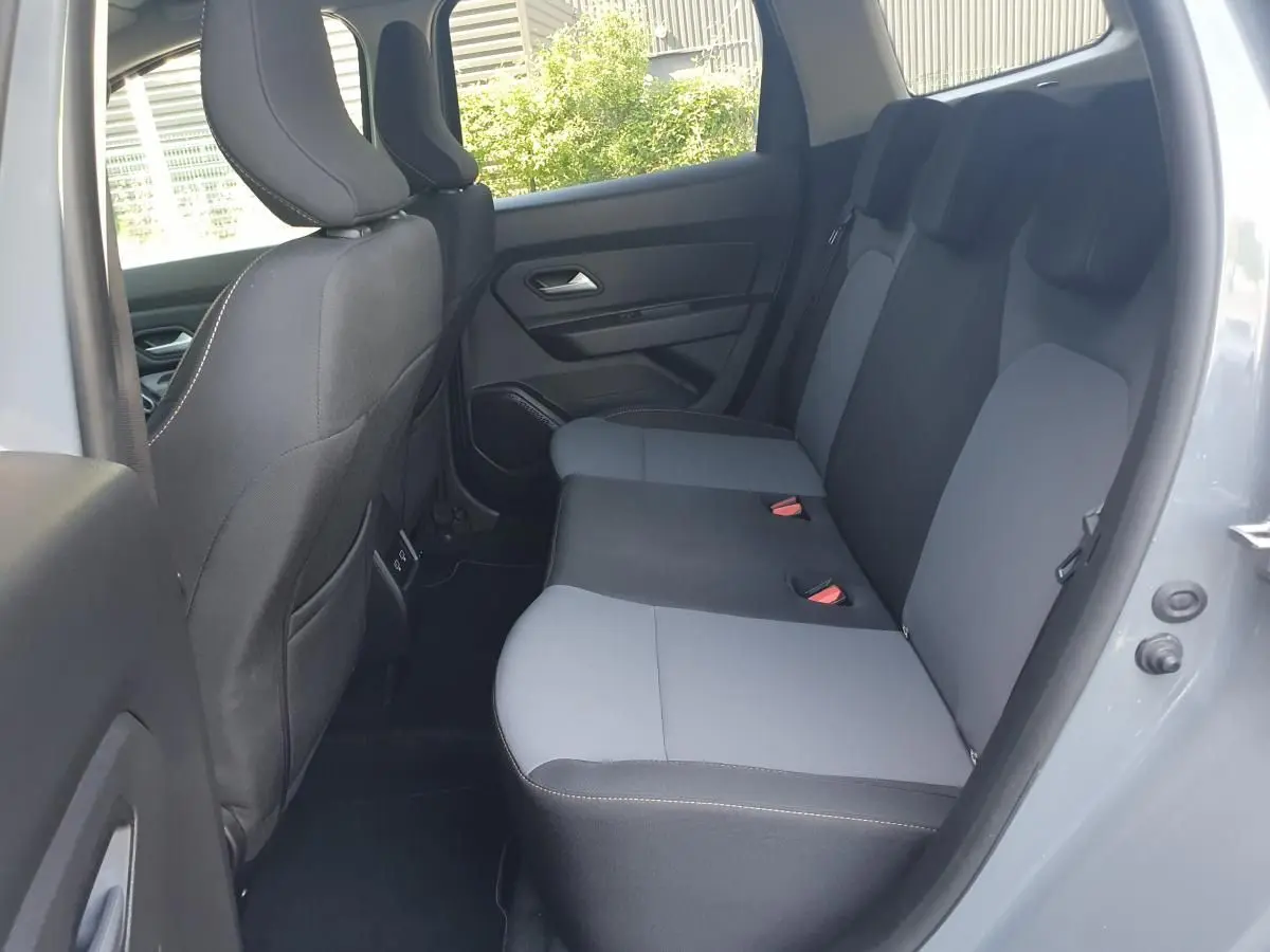 Vue intérieure côté droit des sièges arrière gris clair et foncé du Dacia Duster 2023, porte ouverte sur extérieur lumineux.