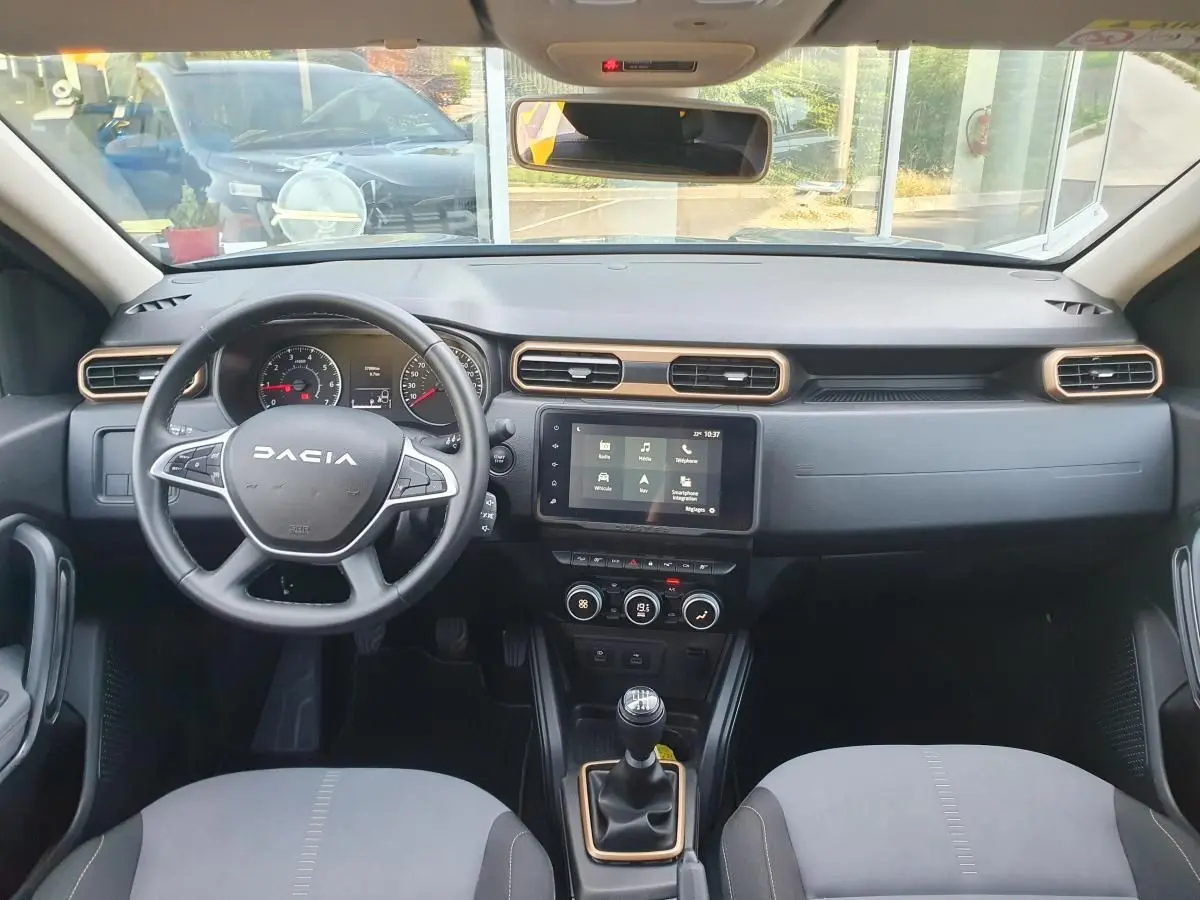 Vue intérieure frontale du tableau de bord du Dacia Duster 2023, avec volant, écran tactile et sellerie gris clair.