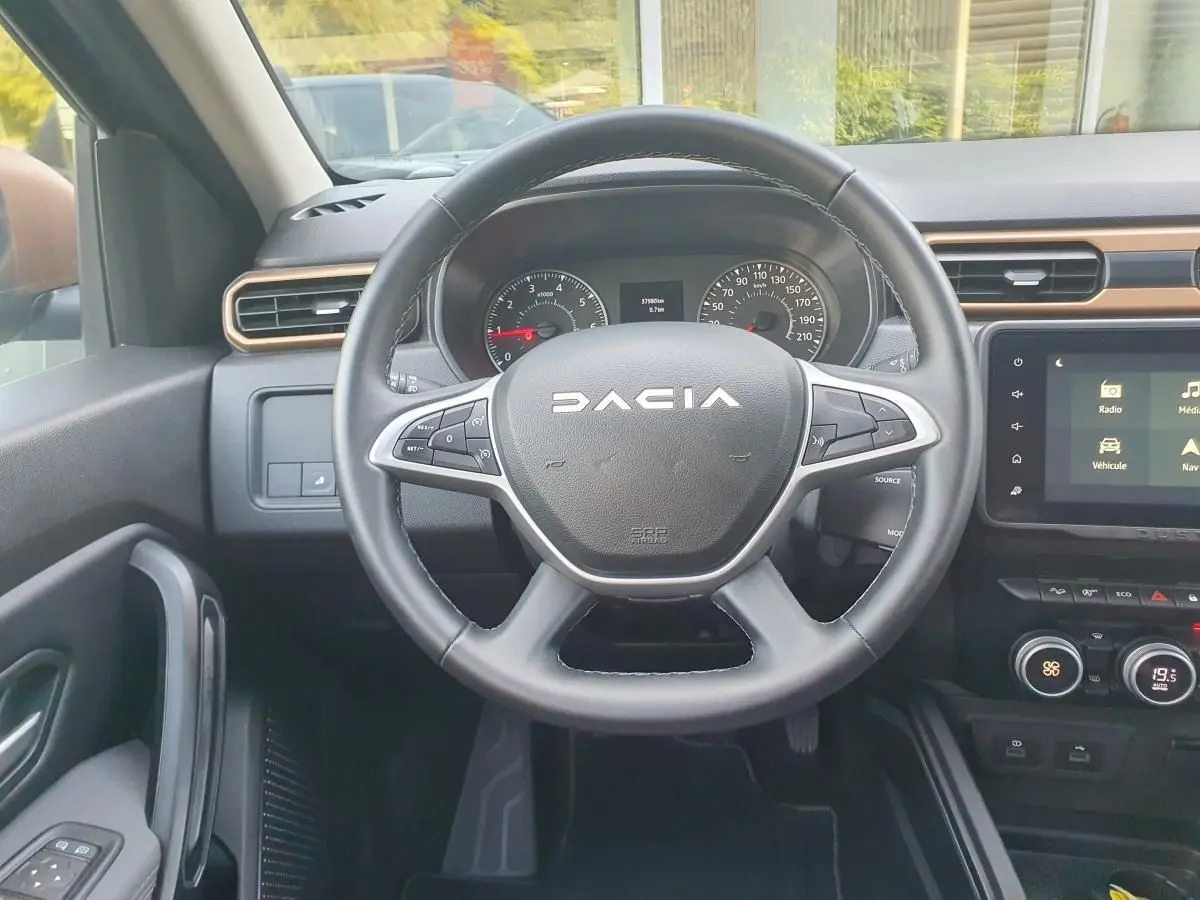 Vue intérieure centrée sur le volant DACIA du Duster 2023 avec tableau de bord et écran tactile visible.
