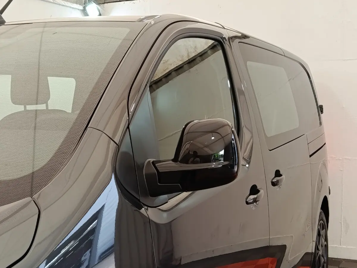Vue de côté droit en gros plan d’un Citroën Jumpy gris foncé avec rétroviseur noir brillant et vitres teintées.