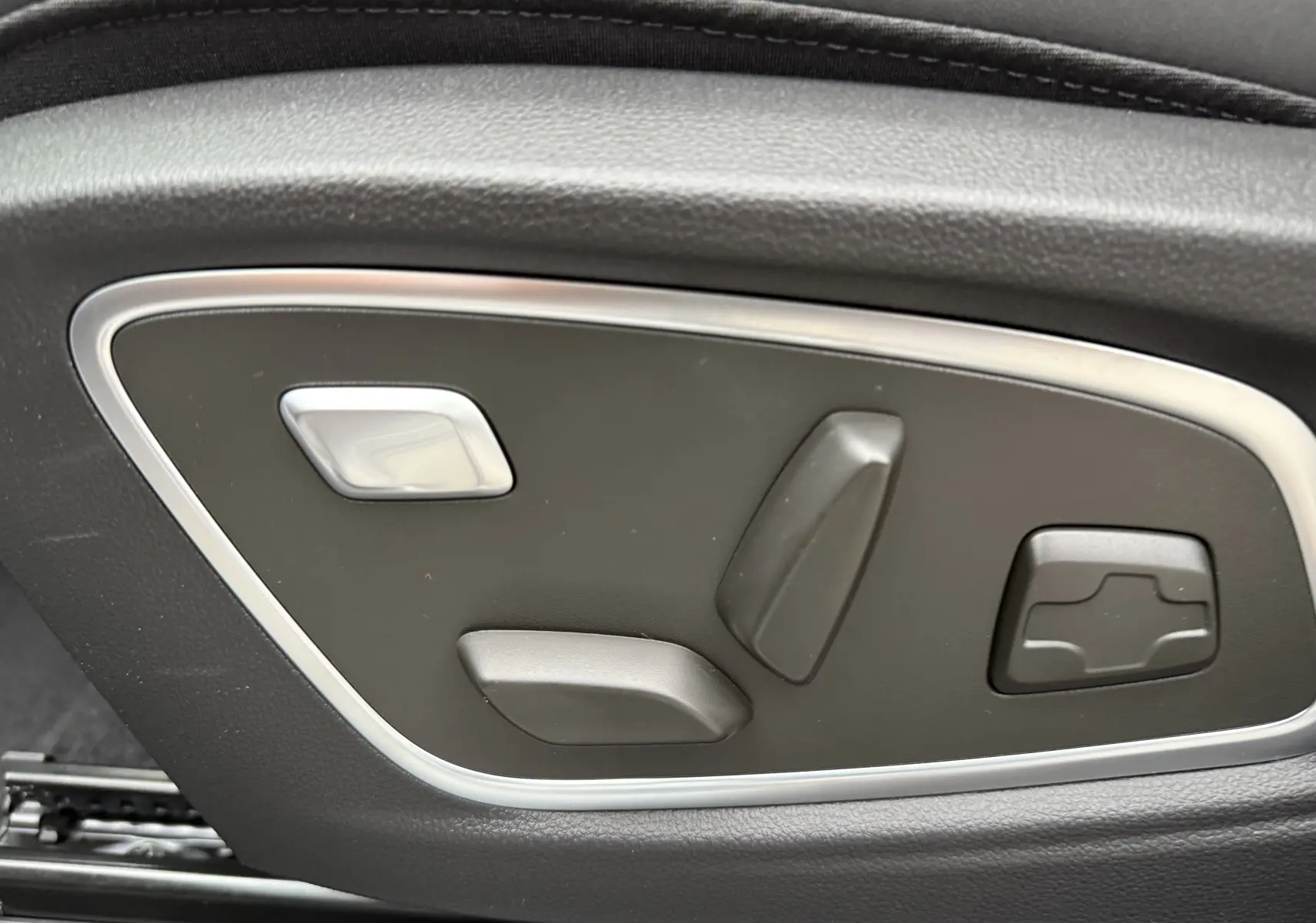 Gros plan sur les commandes électriques de réglage du siège côté gauche, finition noire avec contour argenté.
