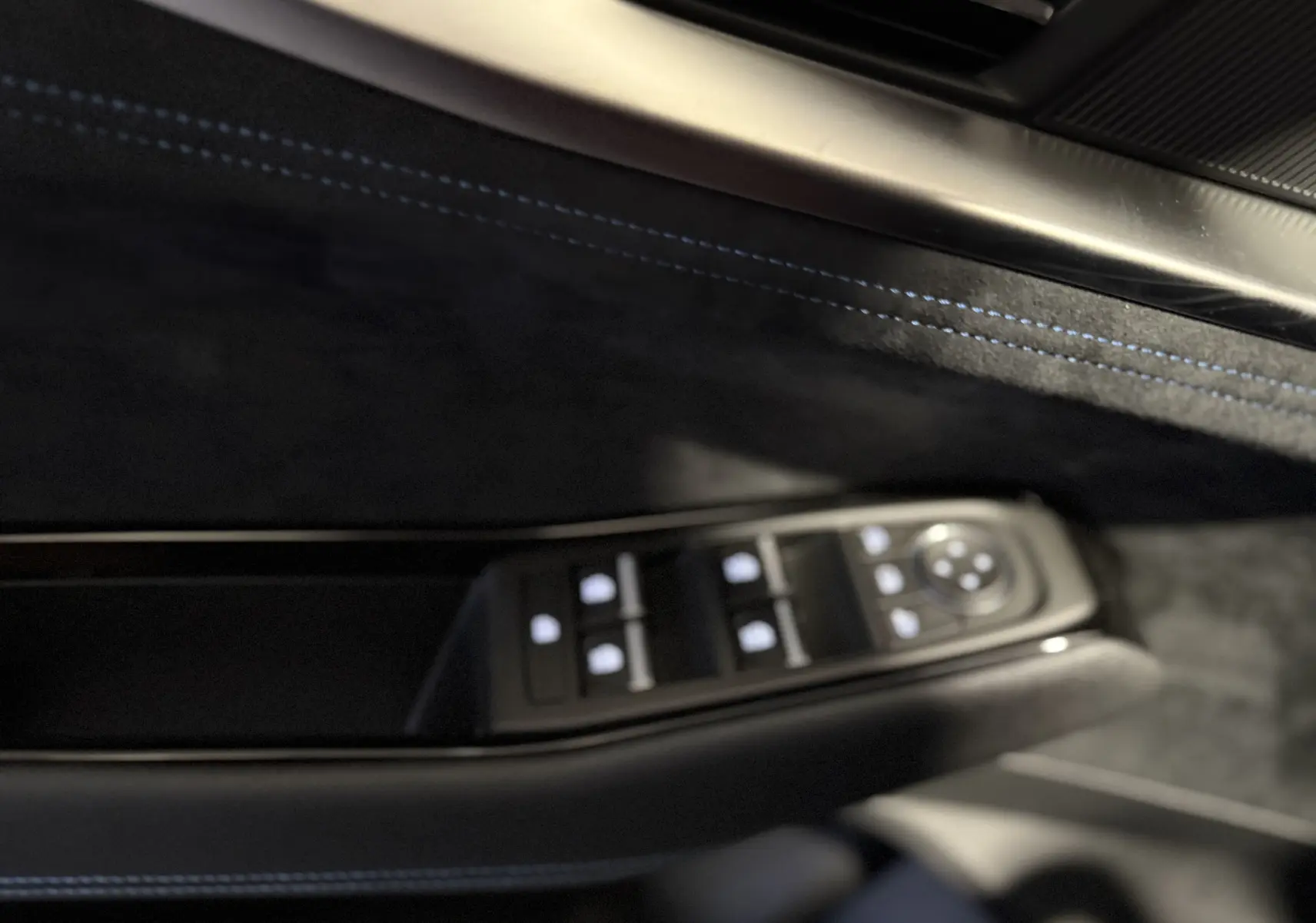 Gros plan sur la commande des vitres côté conducteur du Renault Austral blanc nacré, avec surpiqûres bleues sur la garniture intérieure noire.