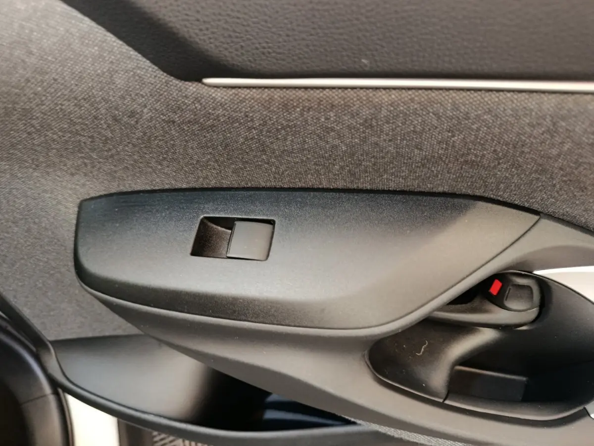 Détail de la commande de lève-vitre côté conducteur noir dans l'habitacle de la Toyota Yaris Cross blanche.