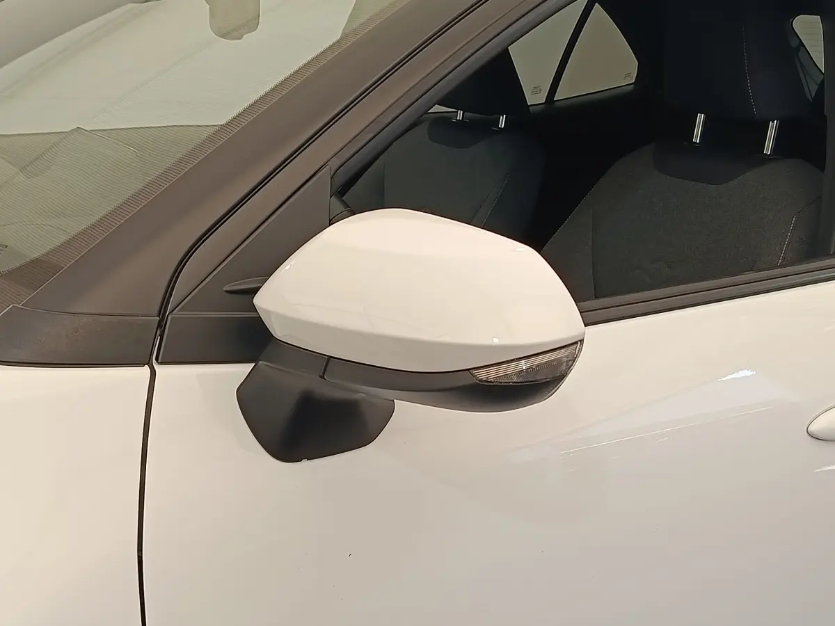 Gros plan sur le rétroviseur côté gauche d'une Toyota Yaris Cross blanche, avec partie de la porte et siège conducteur visibles.