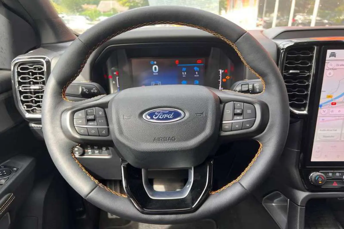 Vue rapprochée du volant cuir noir avec surpiqûres orange du Ford Ranger 2026, tableau de bord digital et écran tactile visibles.