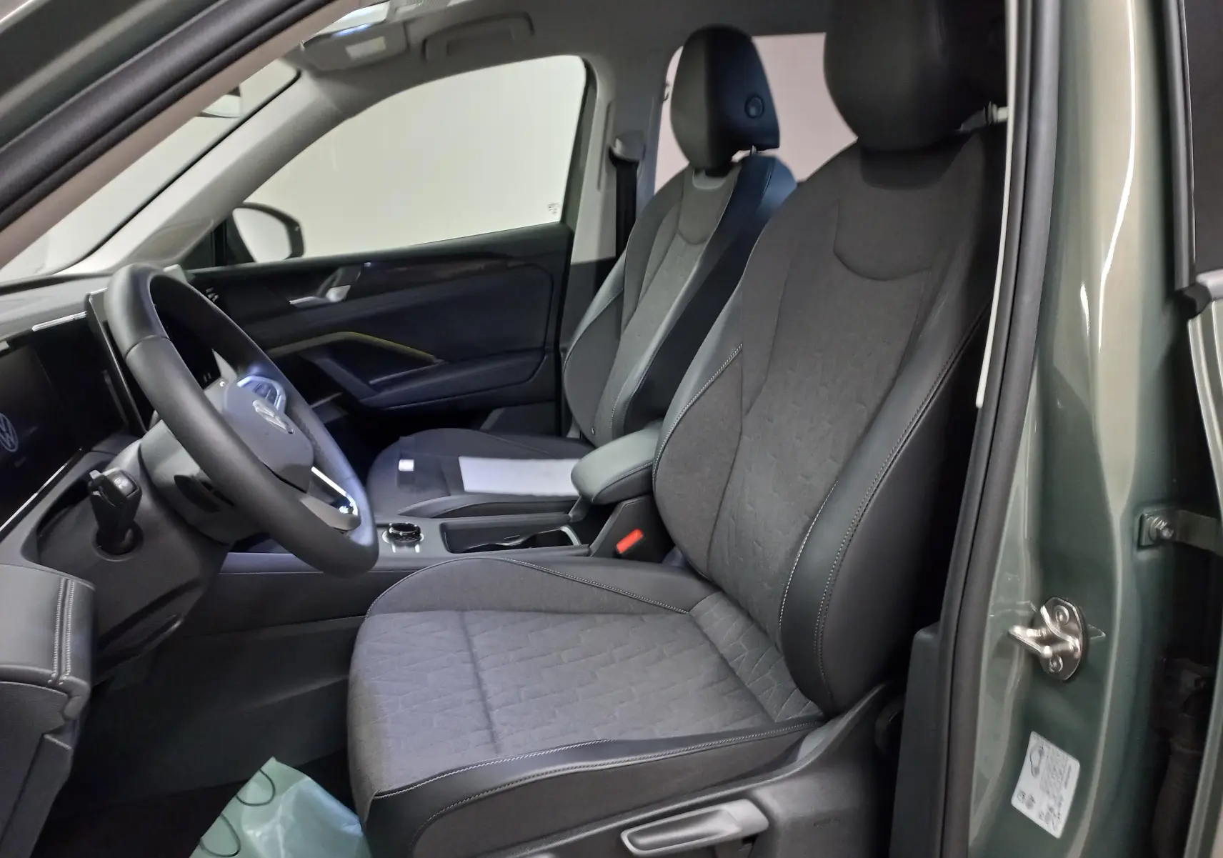 Vue intérieure côté conducteur du Volkswagen Tiguan 2025 vert Cipressino, sièges tissu noir et tableau de bord moderne.