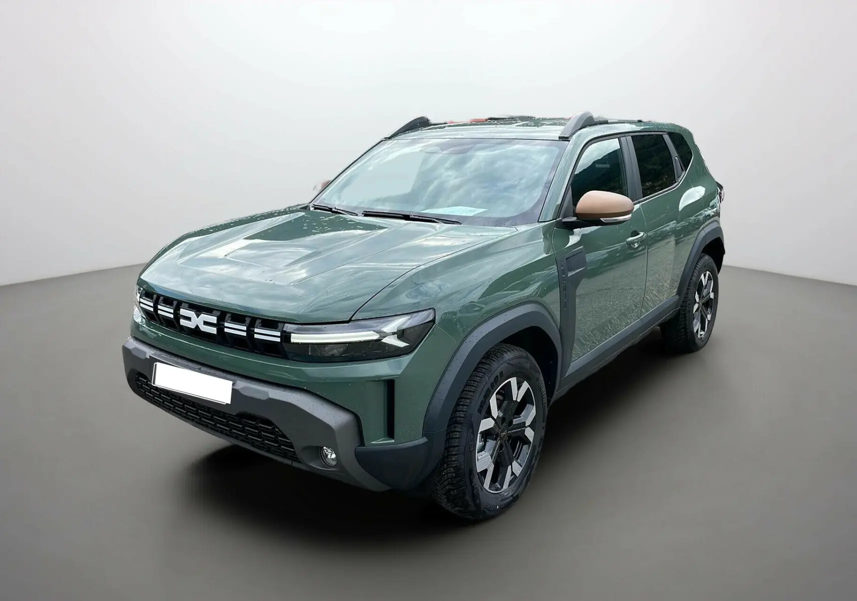 Vue 3/4 avant du Dacia Duster 2025 kaki lichen avec barres de toit et jantes alu 17 pouces, rétroviseurs beige contrastants.