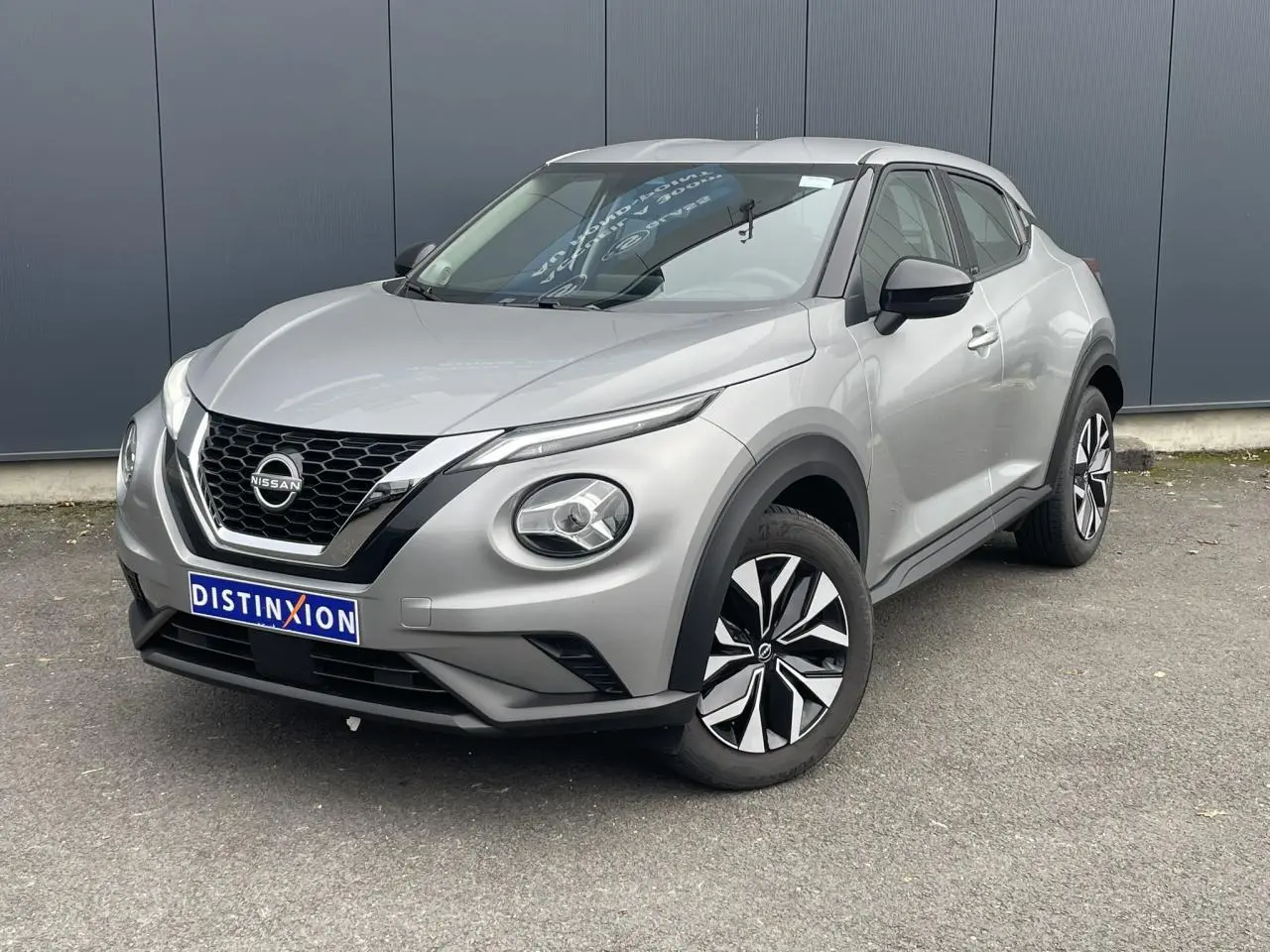 Nissan Juke gris silver en 3/4 avant droit, avec calandre noire et jantes bicolores distinctives.