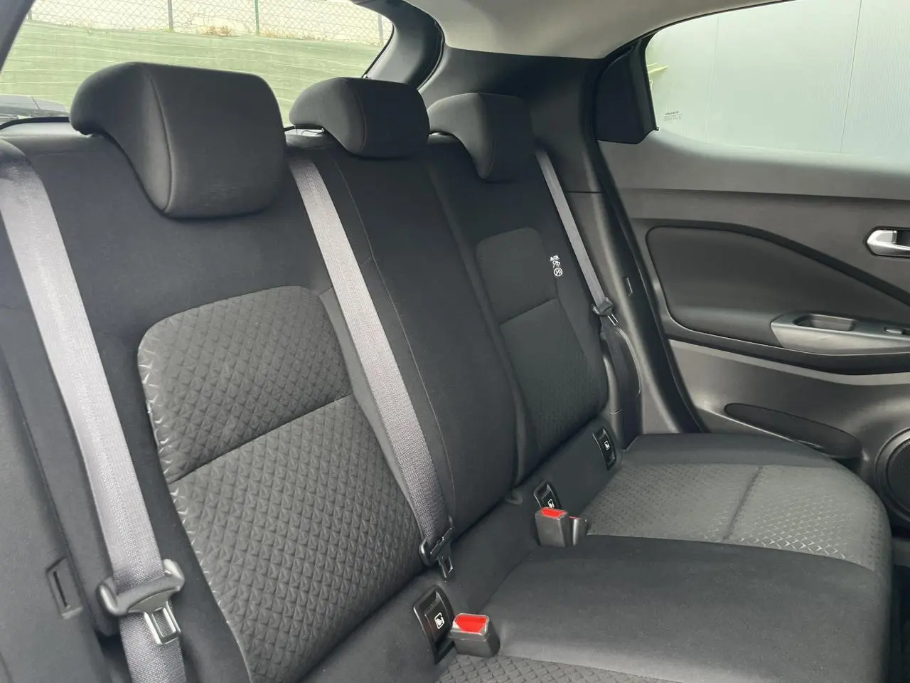 Vue latérale droite des sièges arrière noirs du Nissan Juke 2024, avec ceintures grises et tissu texturé.