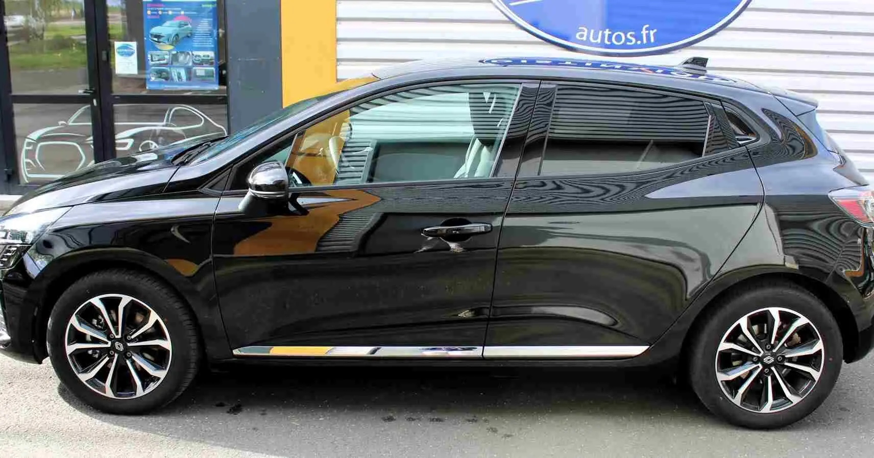 Profil côté gauche de la Renault Clio noire étoile métal 2025 avec jantes alliage bicolores et poignées de porte chromées.