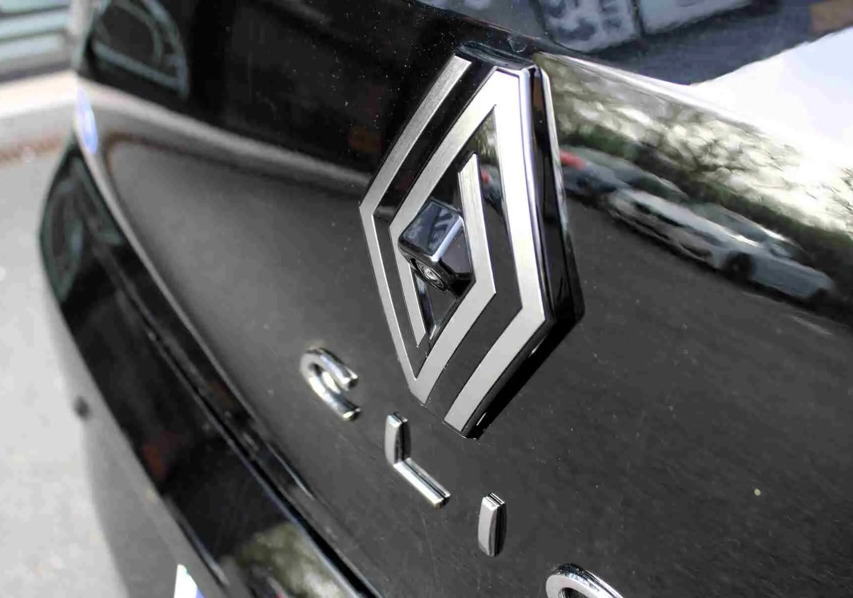 Gros plan sur le logo Renault et l'inscription Clio sur la malle arrière noire étoile métal brillante.