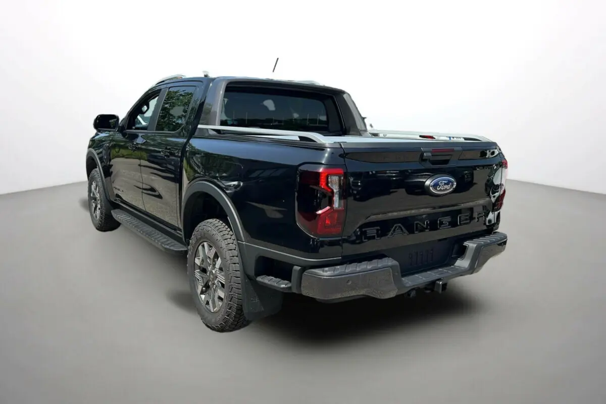 Ford Ranger 2.3 PHEV Wildtrak Plus noir agate, vue 3/4 arrière droit avec benne et barres de toit visibles.