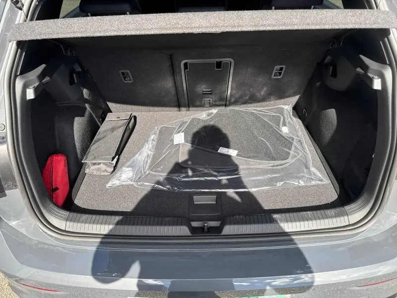 Coffre ouvert vu de l'arrière d'une Volkswagen Golf gris lunaire avec tapis neufs et trappe à skis visible.