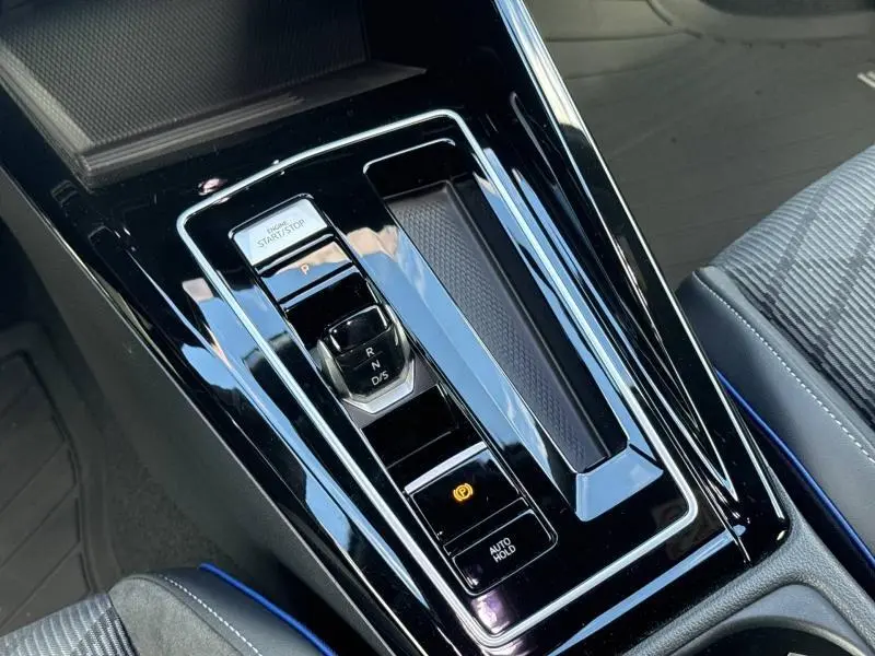 Vue rapprochée de la console centrale noire brillante avec levier de vitesses électronique et bouton start/stop d’une Volkswagen Golf gris lunaire.