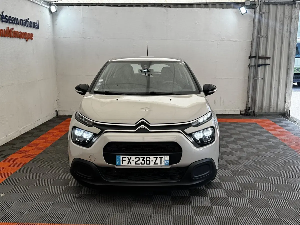 Citroën C3 beige vue de face en intérieur, avec phares LED allumés et calandre noire distinctive.