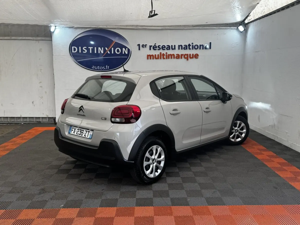 Vue 3/4 arrière droite d'une Citroën C3 beige 2021 avec feux arrière LED et jantes alliage en intérieur showroom.