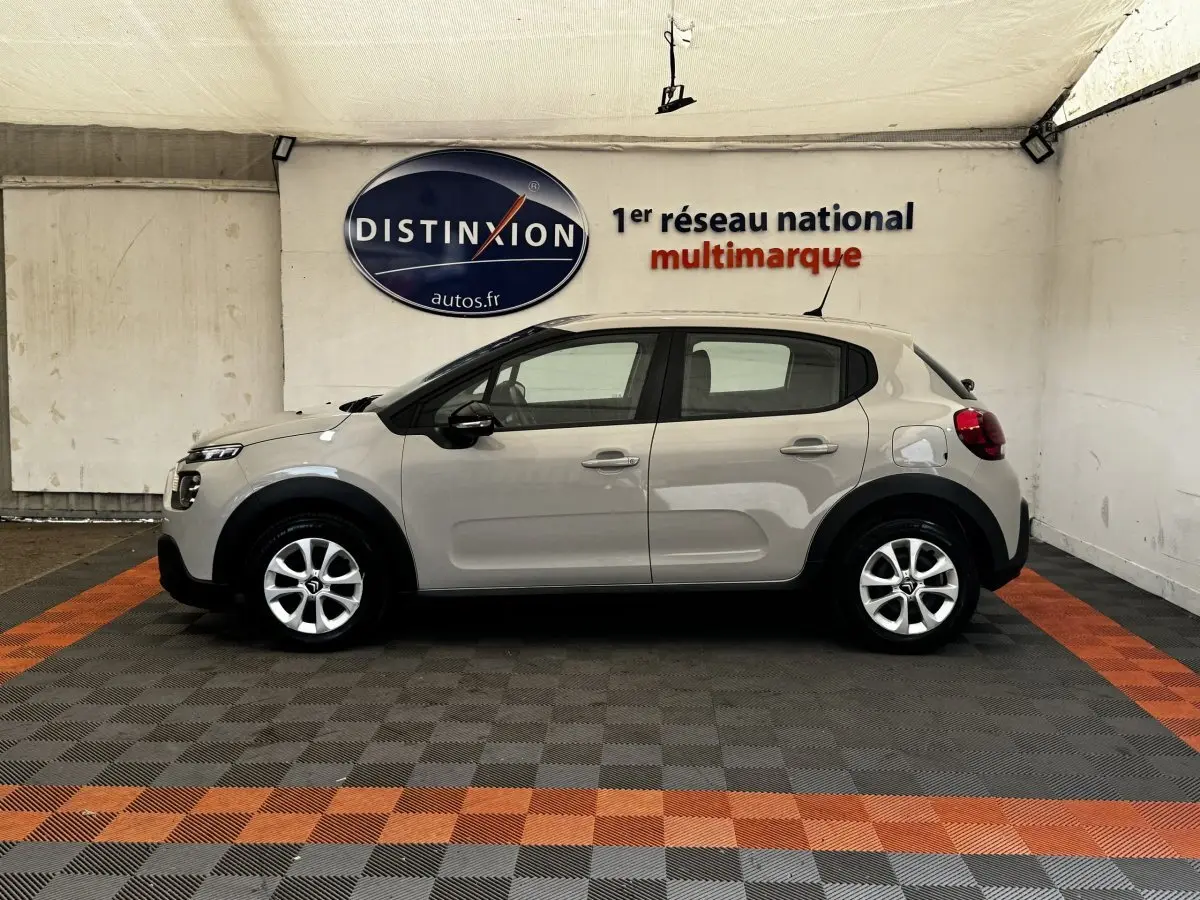 Profil droit d'une Citroën C3 beige 2021 dans un showroom, avec jantes alliage et protections noires sur les passages de roues.