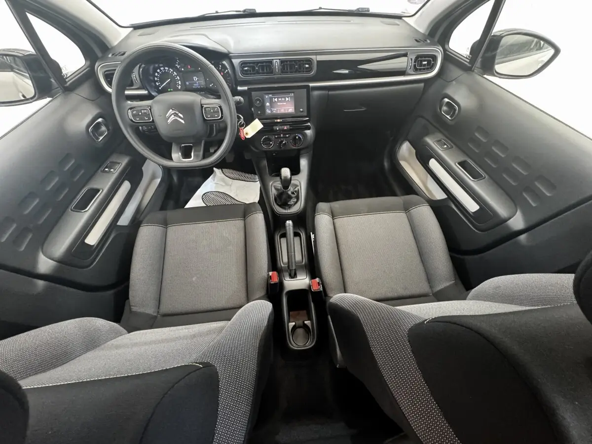 Vue intérieure avant de la Citroën C3 beige 2021, montrant tableau de bord, volant multifonctions et sièges tissu gris.