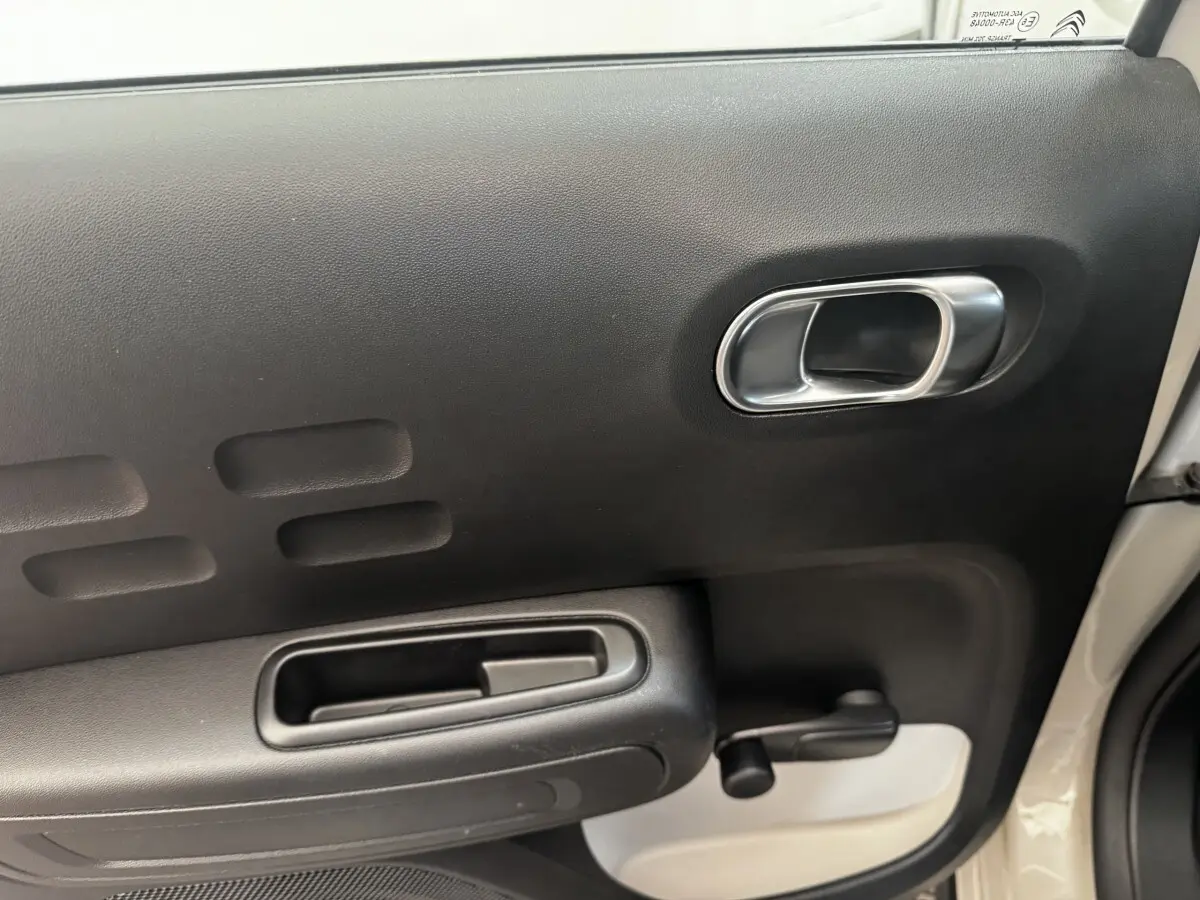 Vue rapprochée de la porte intérieure côté droit de la Citroën C3 beige, avec poignée argentée et manivelle de vitre.