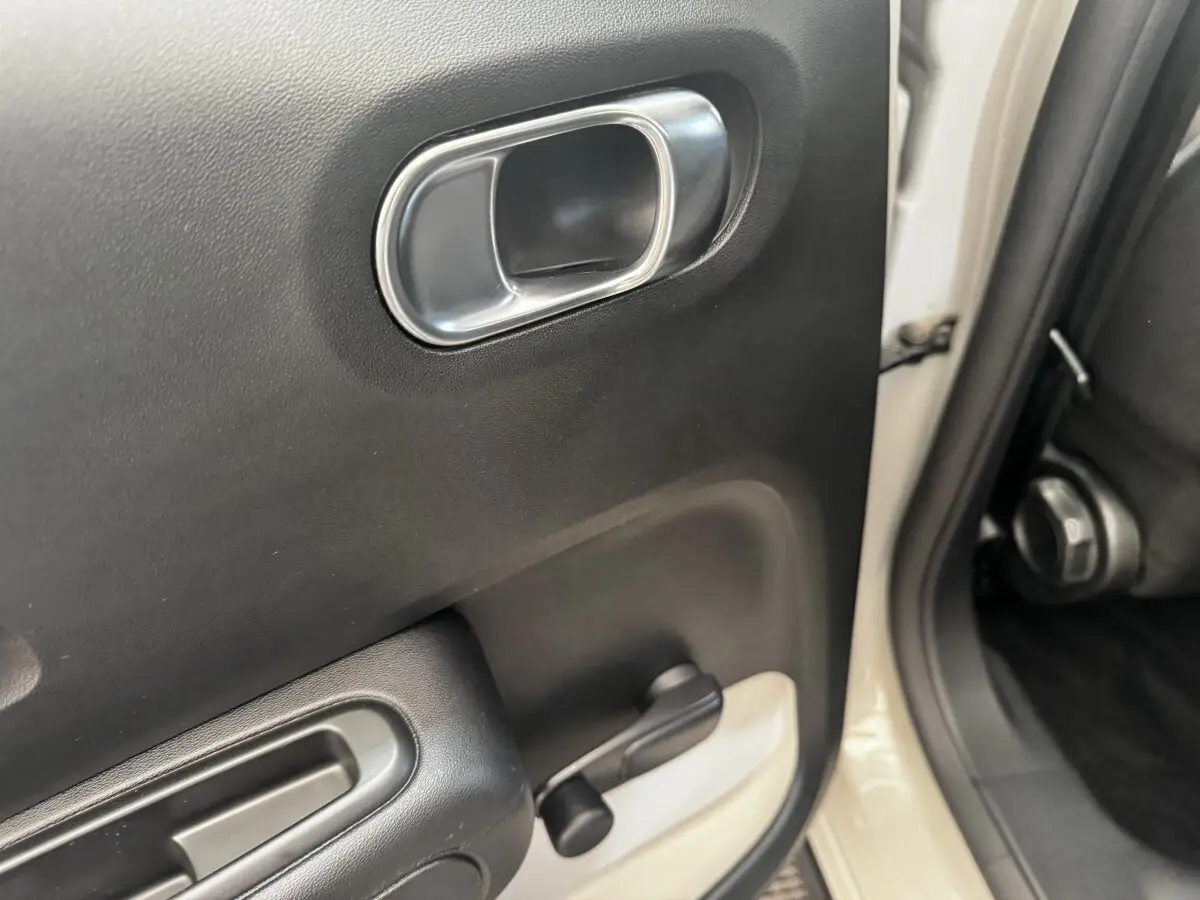 Gros plan sur la poignée intérieure et la manivelle de lève-vitre côté arrière droit d'une Citroën C3 beige.