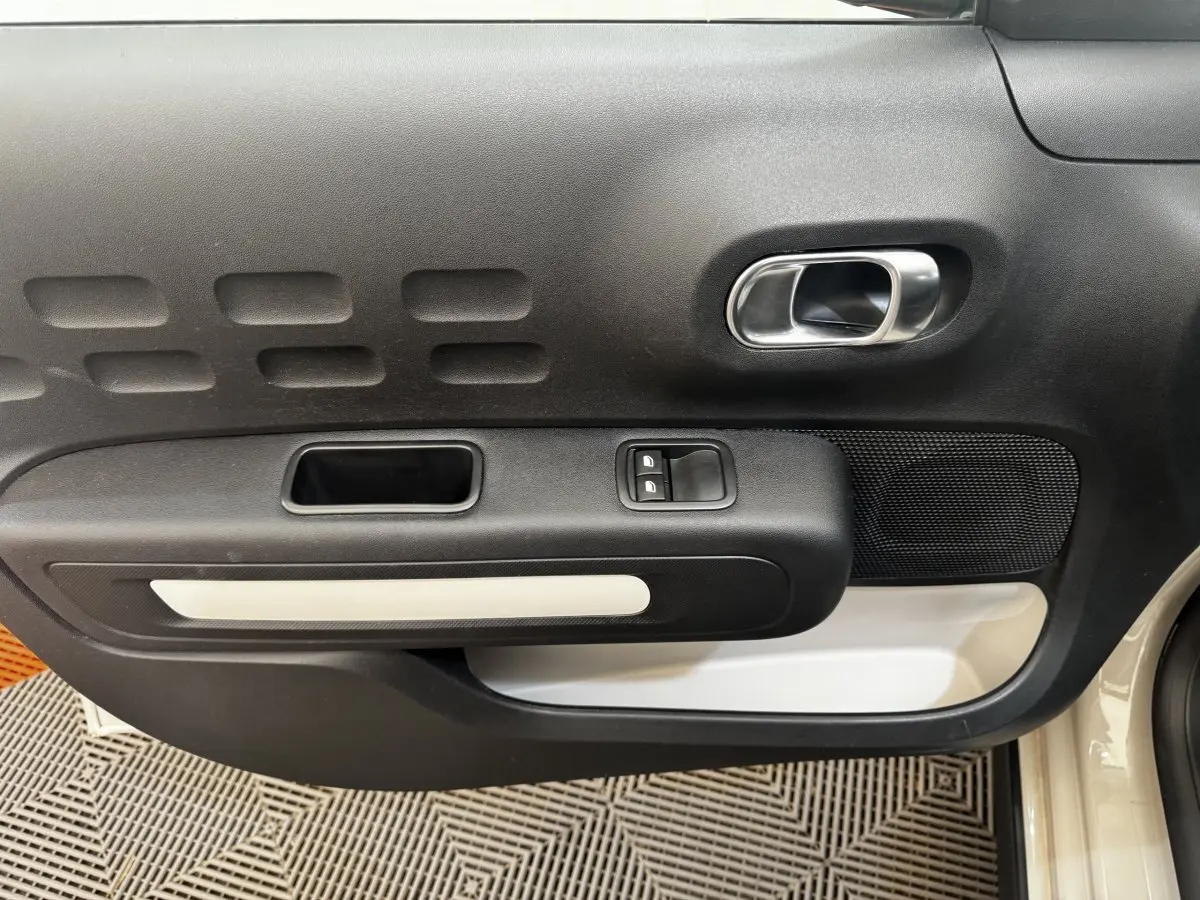Vue rapprochée de la porte avant droite beige de la Citroën C3 avec poignée intérieure chromée et commandes de vitres.