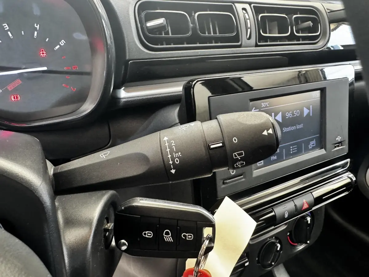Gros plan sur le tableau de bord et la commande d’essuie-glace de la Citroën C3 beige, avec écran multimédia allumé.