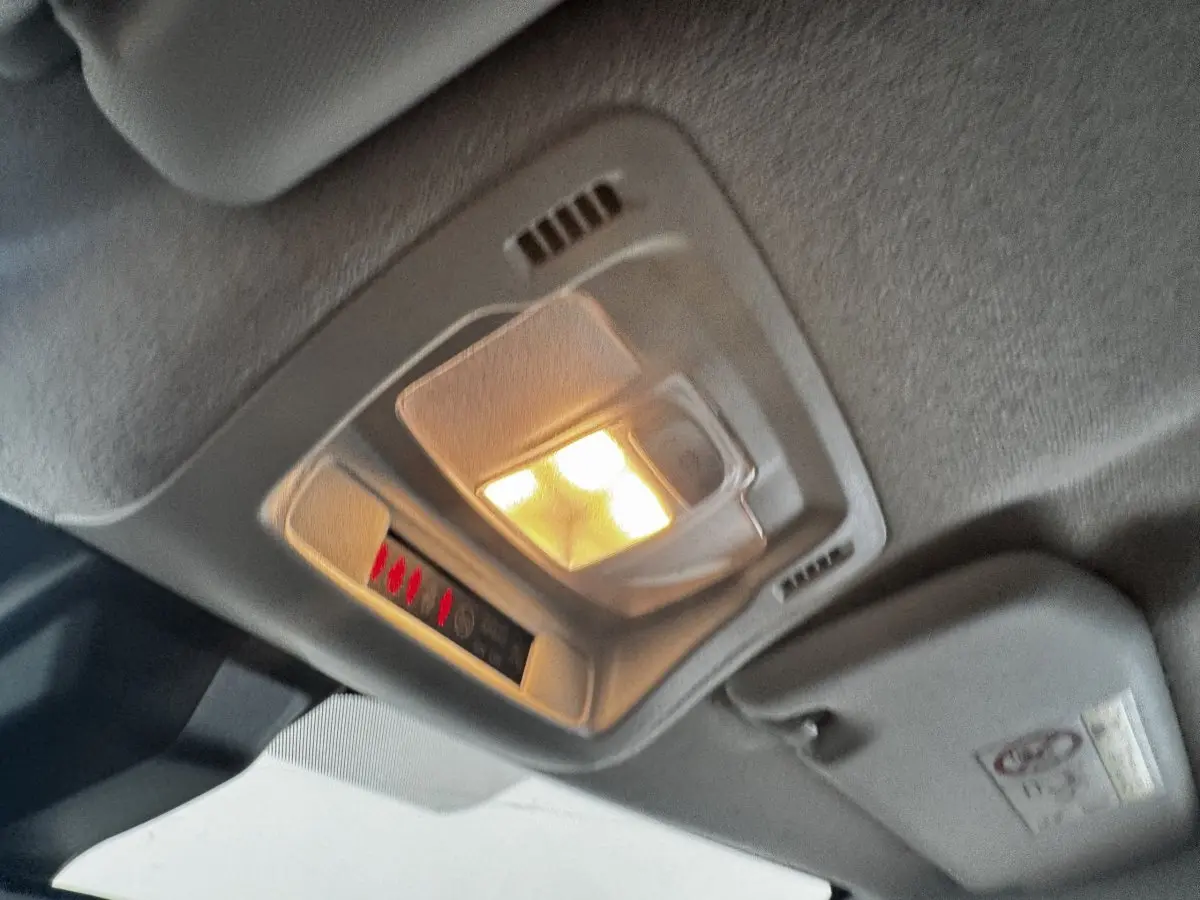 Plafonnier intérieur allumé vu en gros plan dans une Citroën C3 beige, avec pare-soleil et ciel de toit gris.