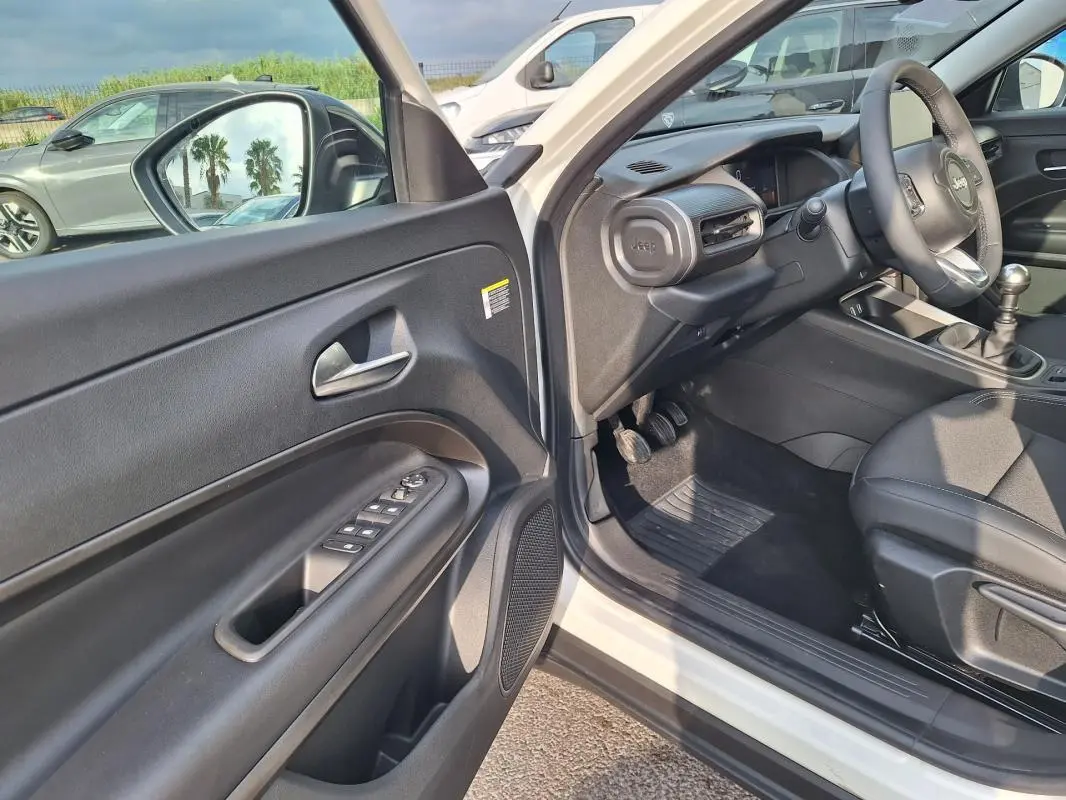 Vue intérieure côté conducteur du Jeep Avenger blanc 2025, montrant porte ouverte et tableau de bord noir.