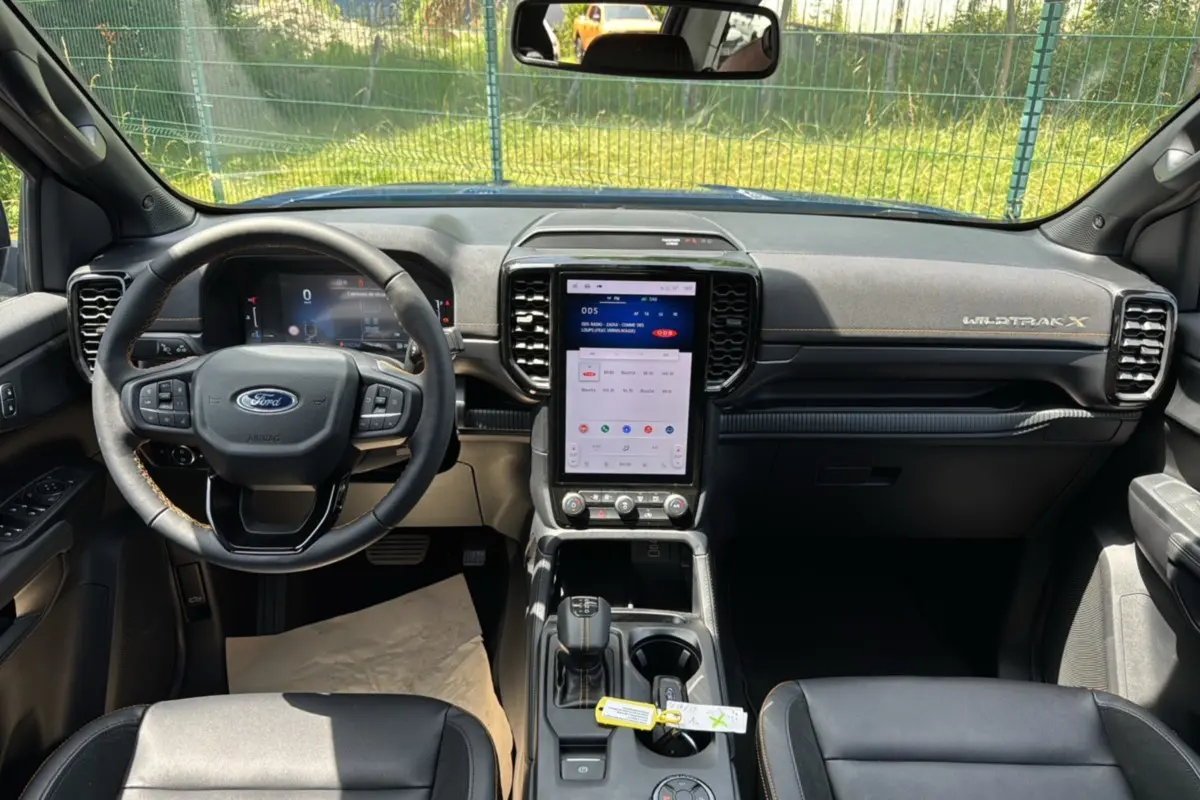 Vue intérieure avant du Ford Ranger Wildtrak X avec tableau de bord noir, volant cuir multifonctions et écran tactile vertical.