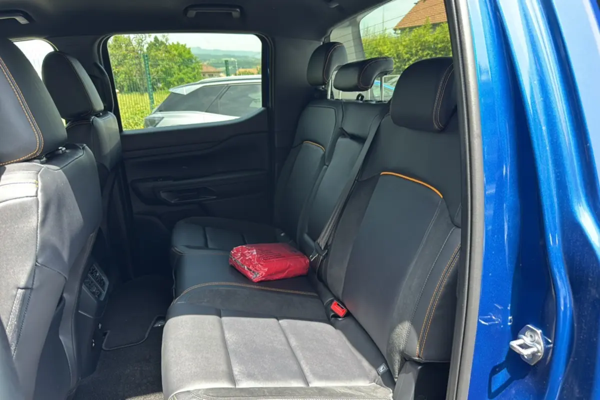 Vue intérieure arrière côté droit du Ford Ranger 205 Wildtrak X bleu lightning avec banquette et un objet rouge posé dessus.