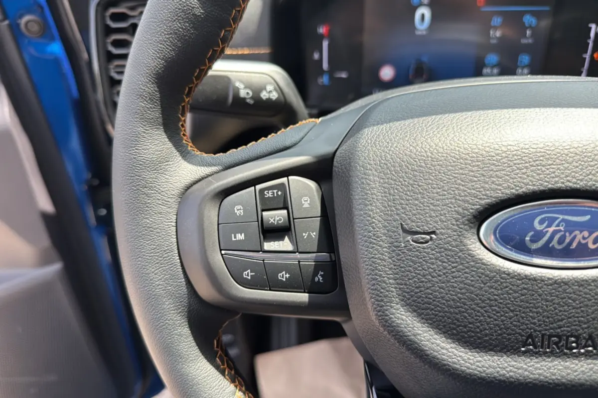 Gros plan sur le volant cuir multifonctions du Ford Ranger bleu lightning, avec commandes de régulateur et logo Ford visible.