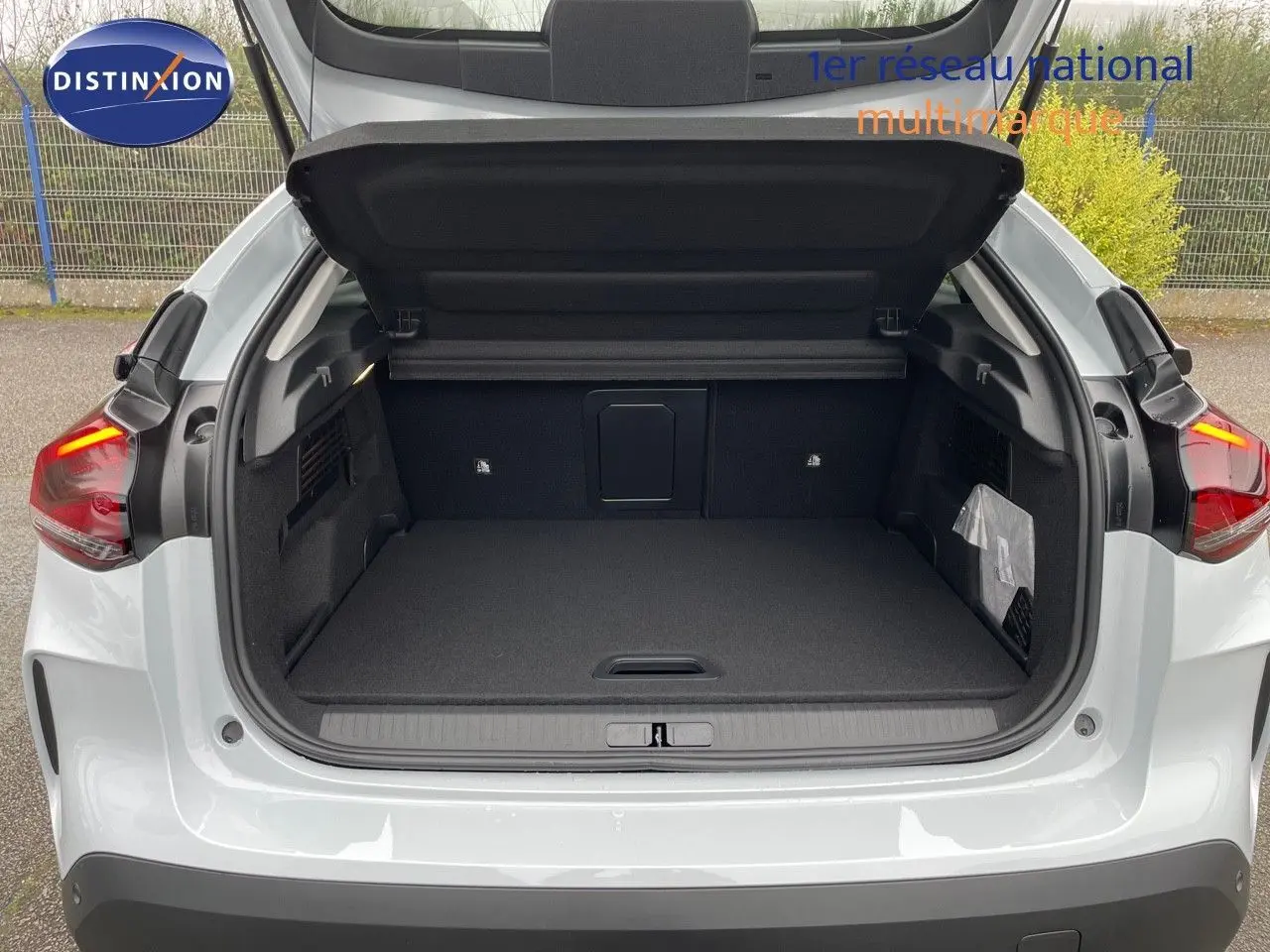 Coffre ouvert vu de l'arrière d'une Citroën C4 blanche métal 2024 avec feux arrière allumés.