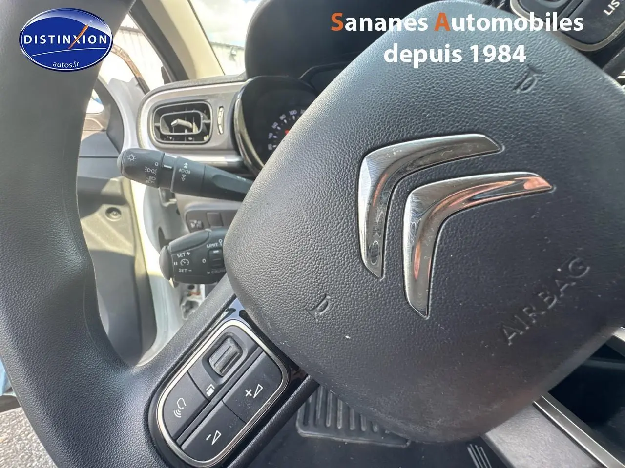 Gros plan sur le volant Citroën C3 blanc, mettant en valeur les commandes audio intégrées et le tableau de bord partiel.