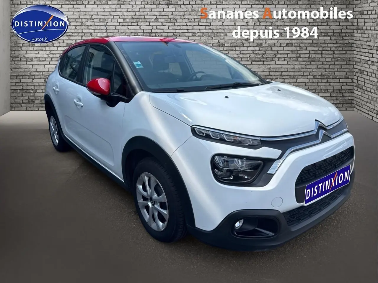 Citroën C3 blanc Banquise avec toit et rétroviseurs rouges, vue 3/4 avant droit sur fond urbain.