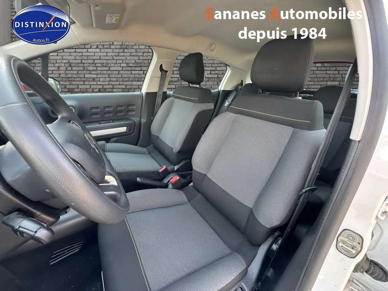 Intérieur de la Citroën C3 2023, vue côté conducteur, sièges tissu gris avec surpiqûres jaunes et volant noir.