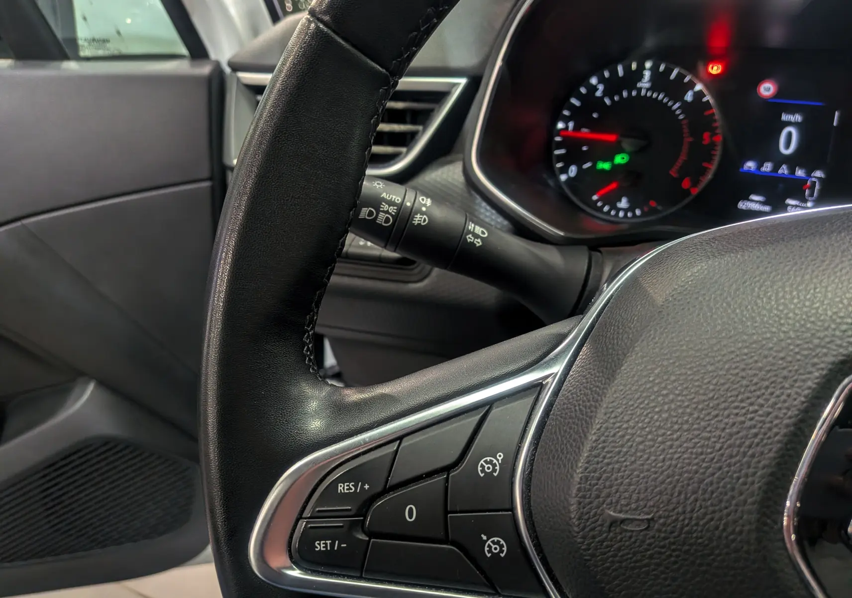 Gros plan sur le volant côté gauche de la Renault Clio V Business 2020, avec commandes de régulateur et tableau de bord allumé.