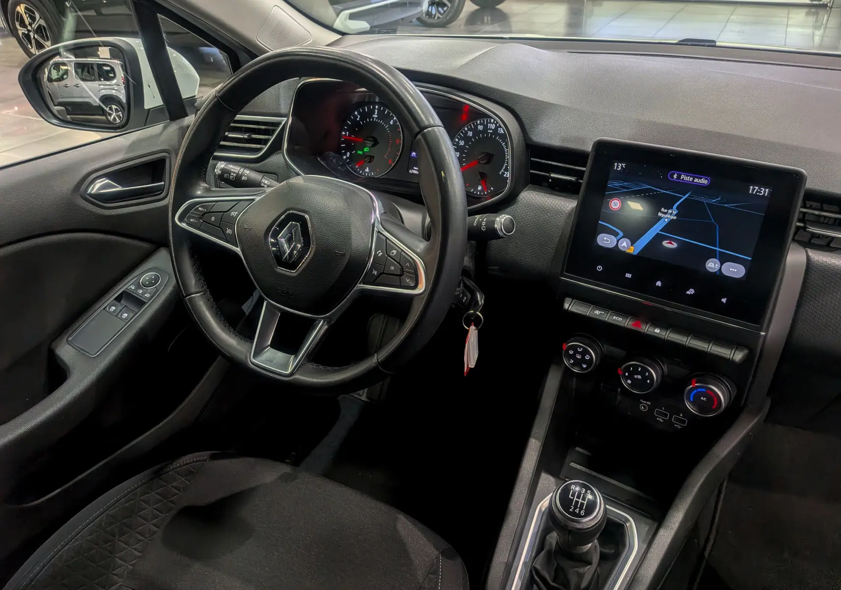 Vue intérieure côté conducteur de la Renault Clio V Business 2020 avec volant multifonction, écran tactile et levier de vitesse manuel.