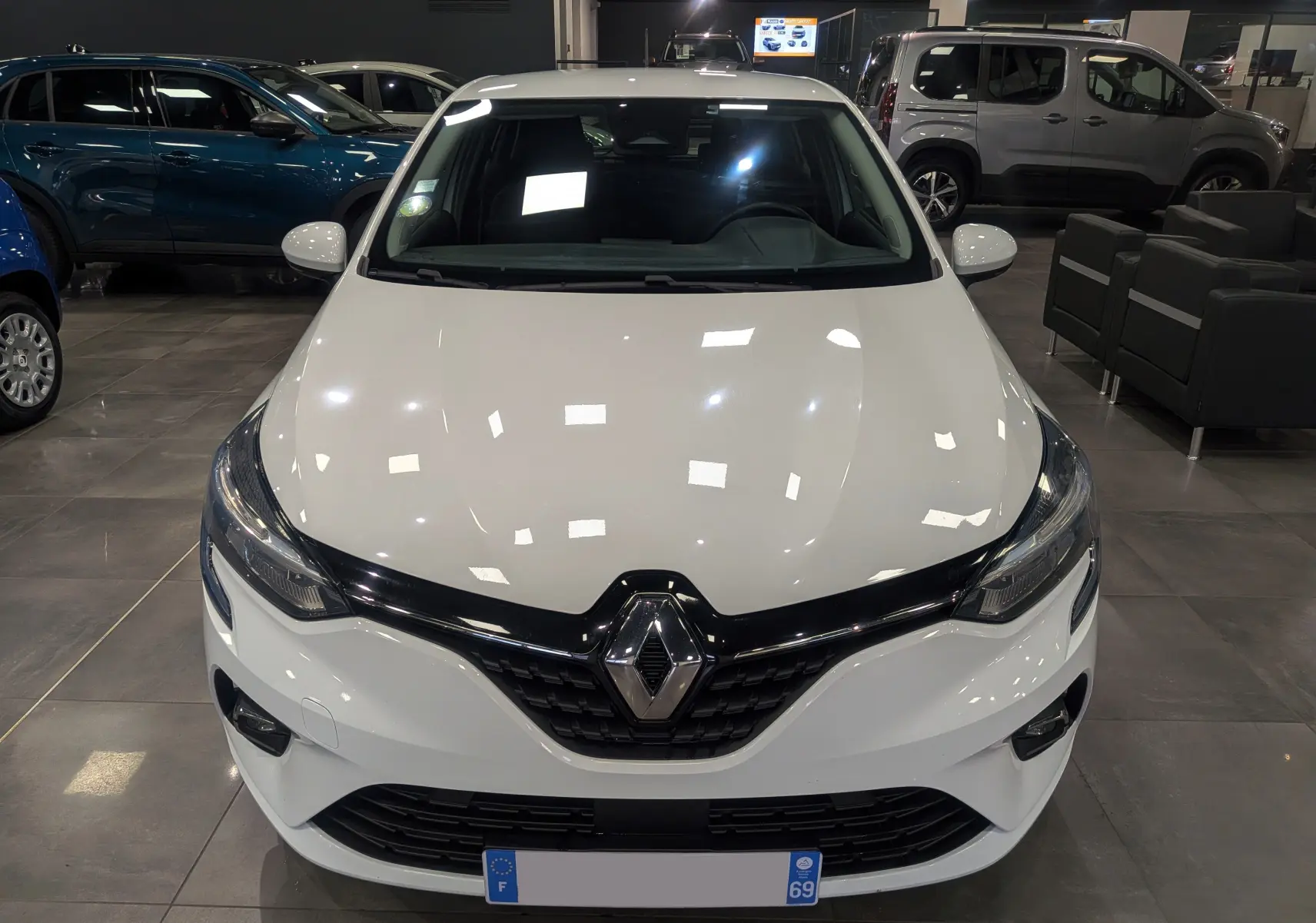 Vue avant d'une Renault Clio V Business blanche Glacier, avec calandre noire brillante et phares LED en showroom.