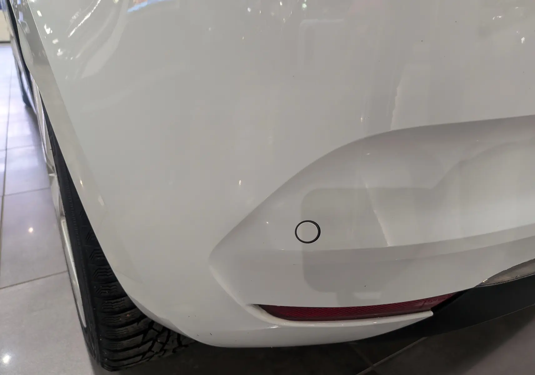 Gros plan sur le pare-chocs arrière droit blanc glacier d'une Renault Clio V Business 2020 avec capteur de recul visible.